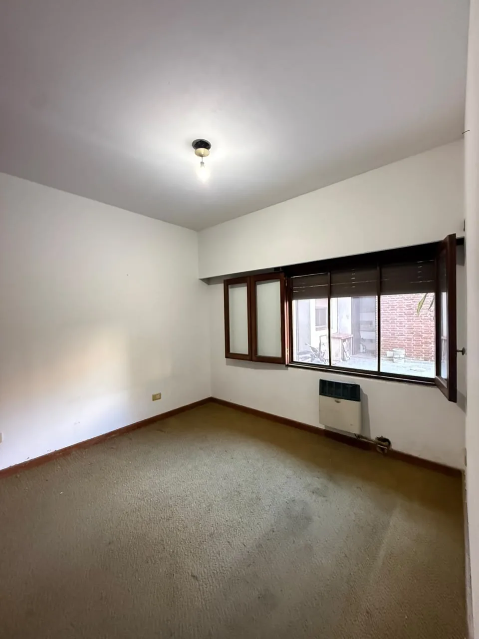 Ambiente alfombrado, con ventana al patio y calefactor