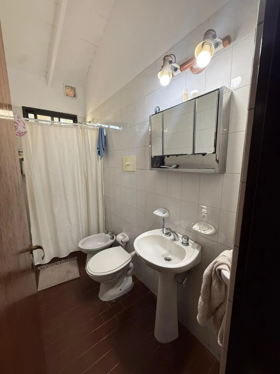 Baño completo revestido en blanco, con ducha y botiquín