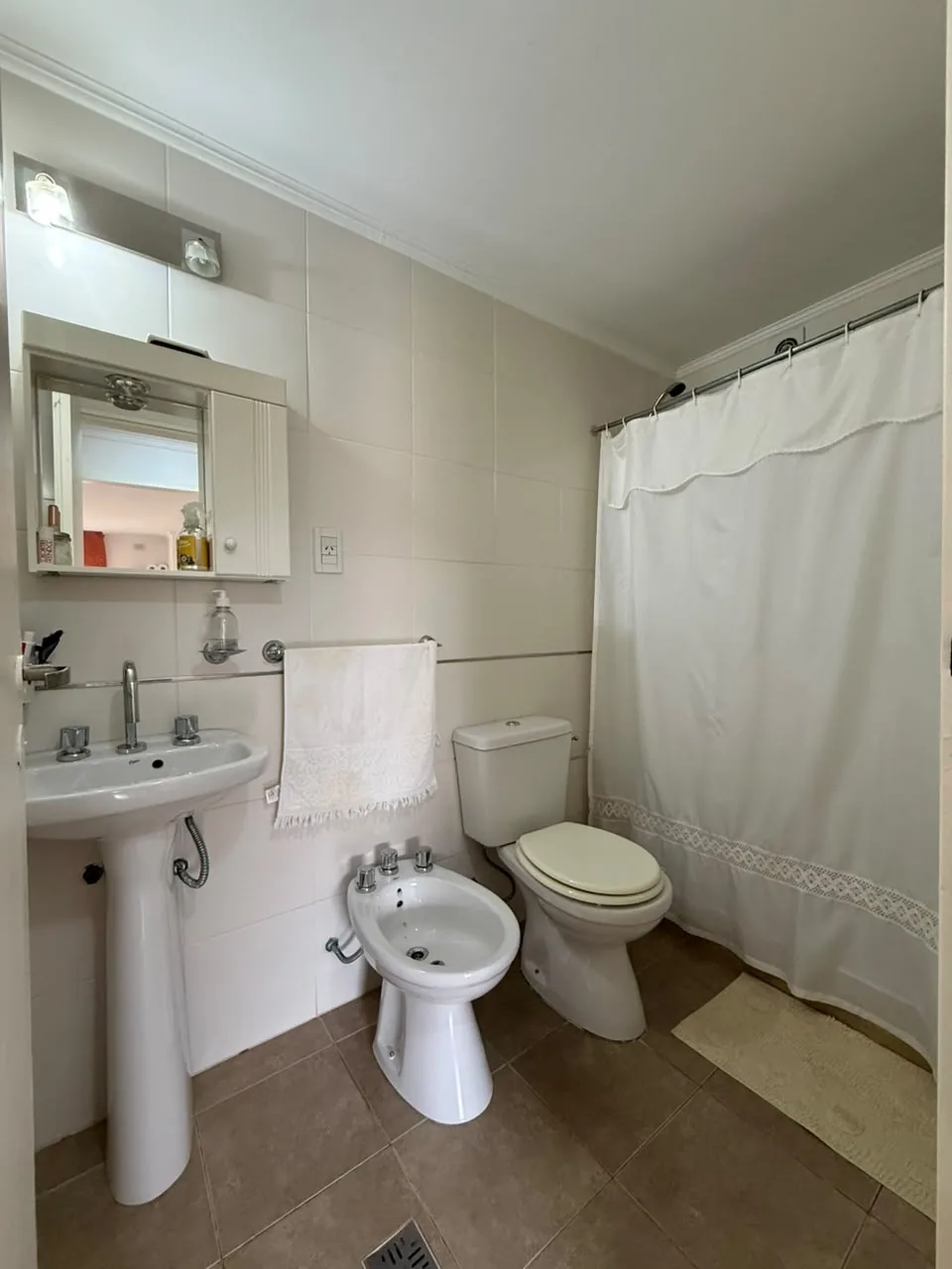 El baño completo, revestido en cerámica, con lavatorio de pie, inodoro, bidet y botiquín con espejo
