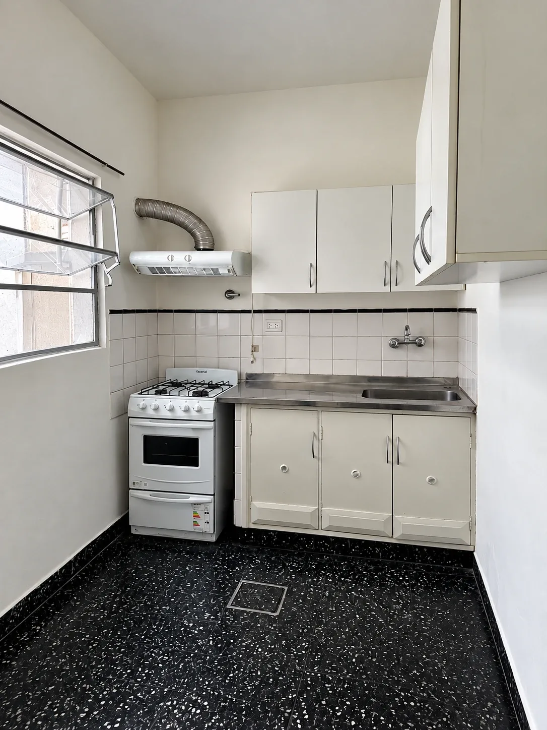 La cocina equipada: cocina con horno, mesada de acero inoxidable con bacha, alacenas y extractor