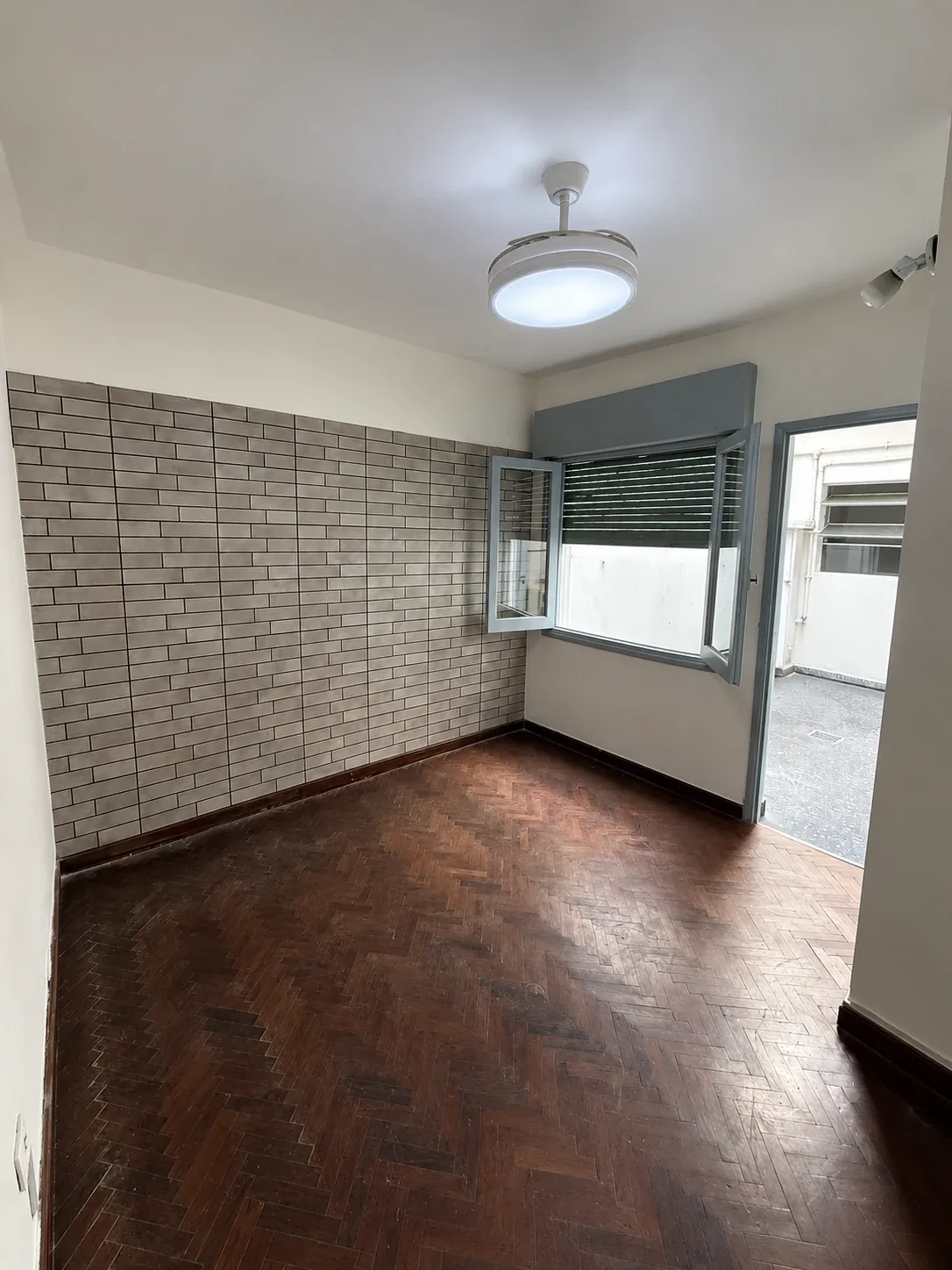 Dormitorio con pared revestida símil ladrillo, ventilador de techo con luz y salida al patio interno