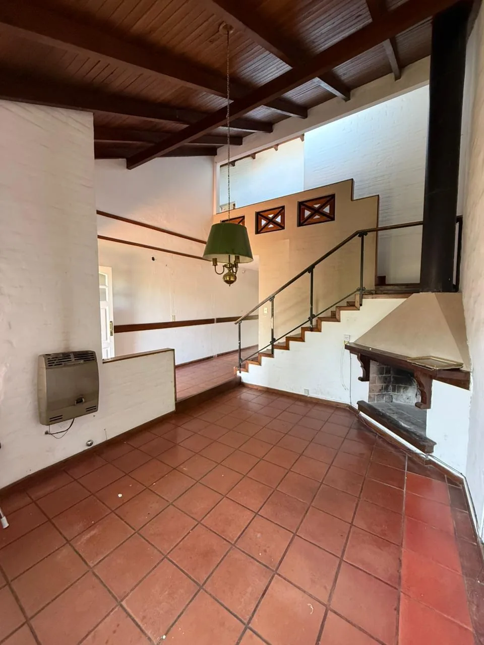 El living, con hogar, techo de madera con vigas a la vista y la escalera