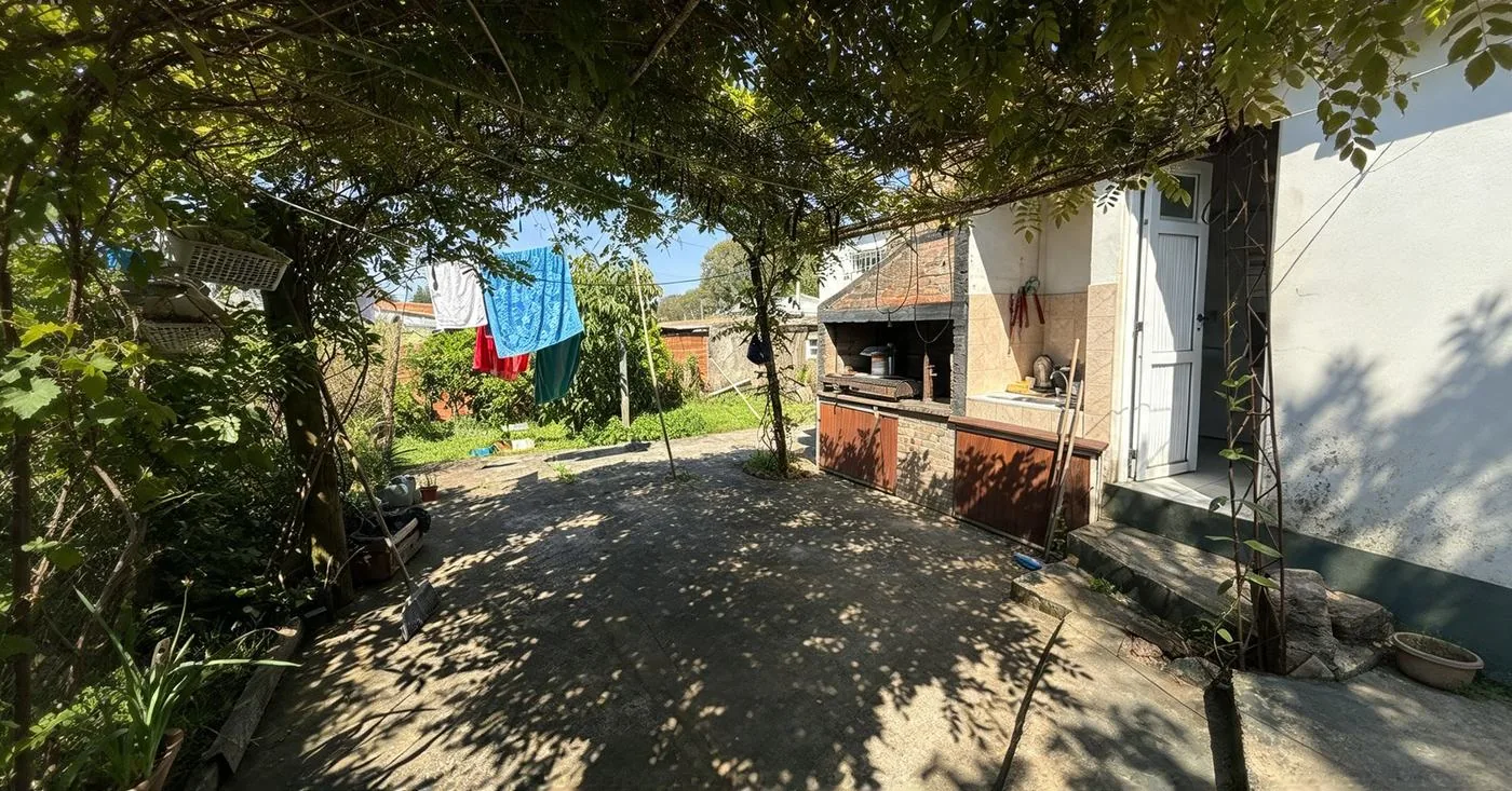 Bajo la pérgola de glicina: la parrilla de obra con mesada y la puerta de servicio