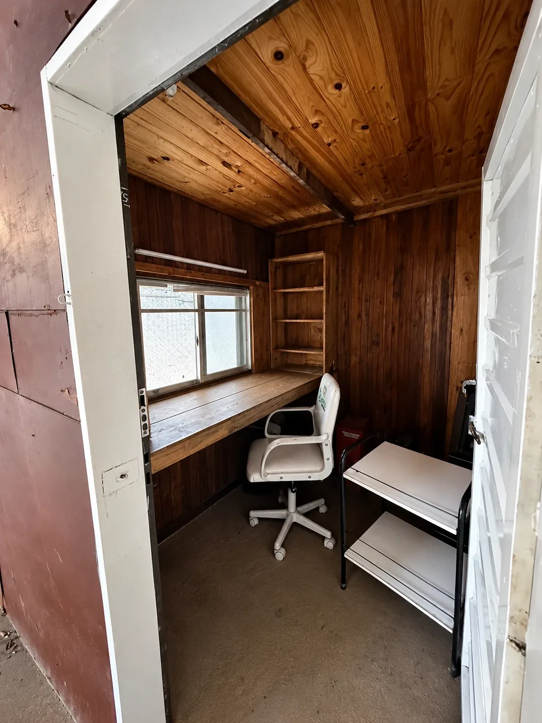 La oficina, revestida en madera, con escritorio fijo y ventana hacia la nave