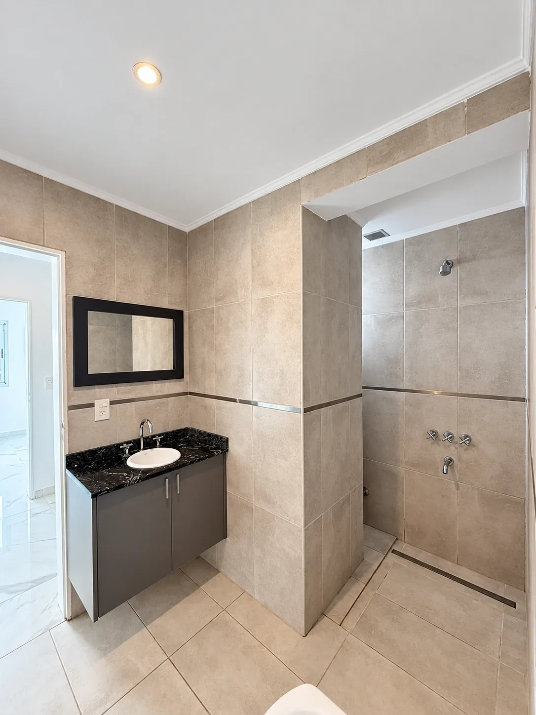 El baño completo: vanitory con mesada de granito, espejo y ducha con rejilla lineal