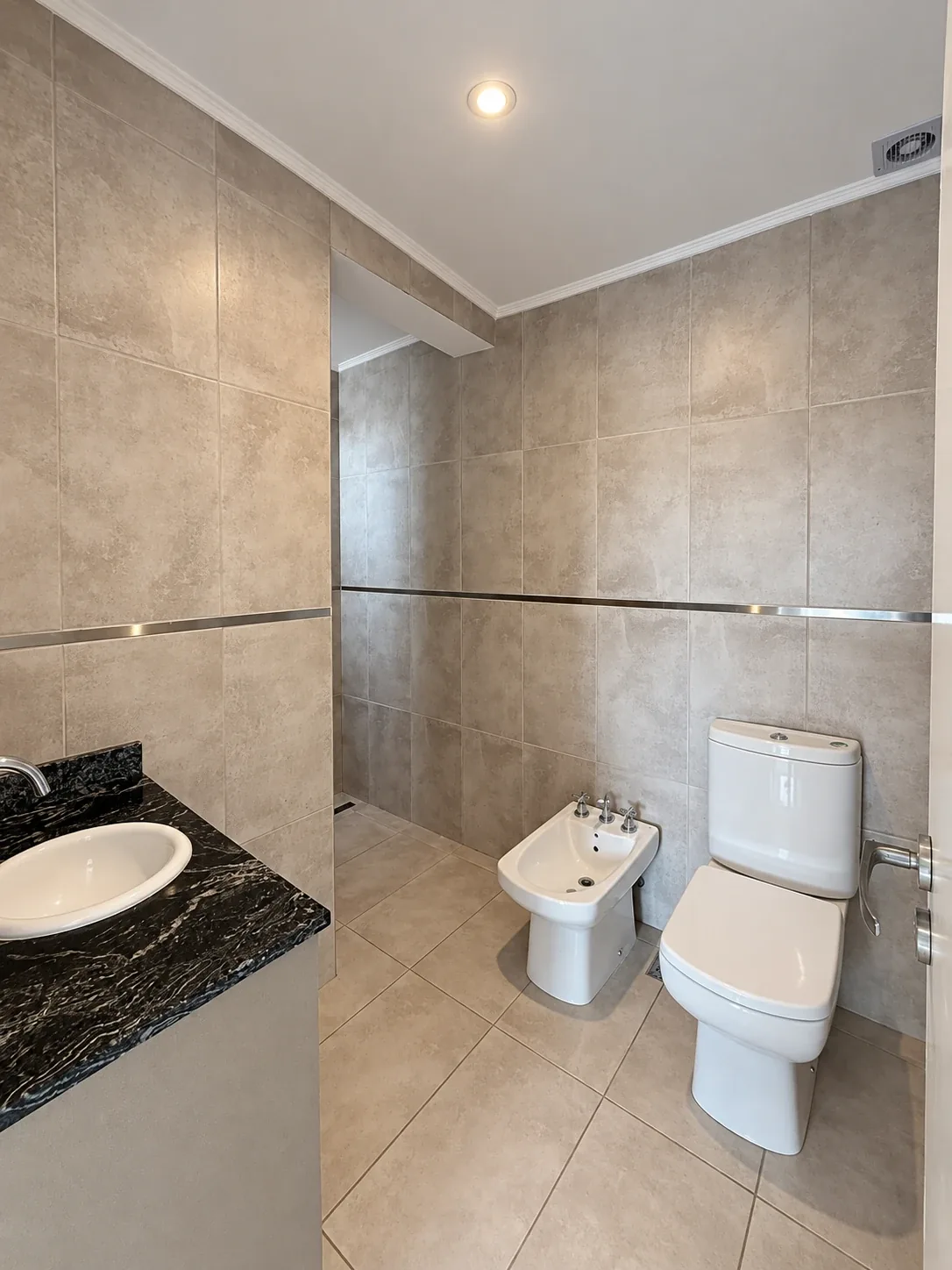 El baño, revestido en porcelanato hasta el techo, con inodoro y bidet