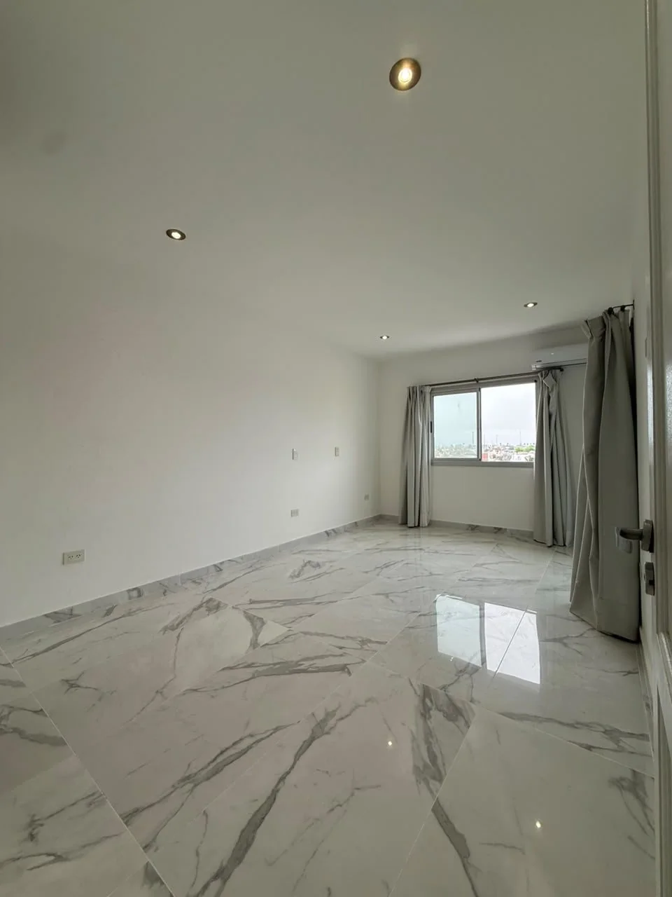 El dormitorio principal, con piso símil mármol, ventana, salida al balcón cerrado y aire acondicionado