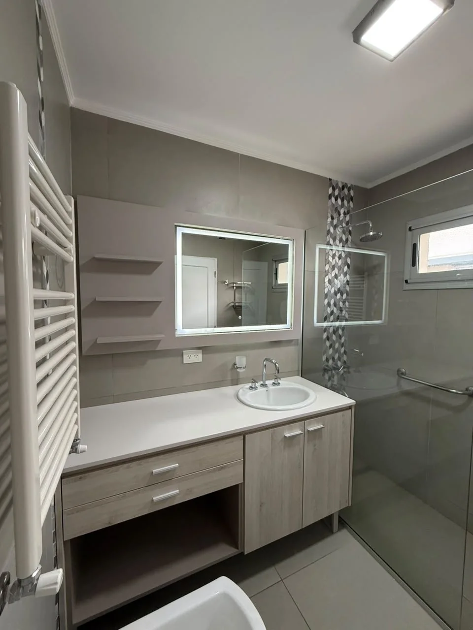 El baño de la suite: vanitory, espejo con luz, toallero calefaccionado y ducha con mampara