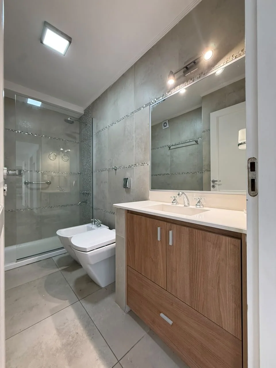 Baño con ducha con mampara de vidrio, vanitory de madera y espejo