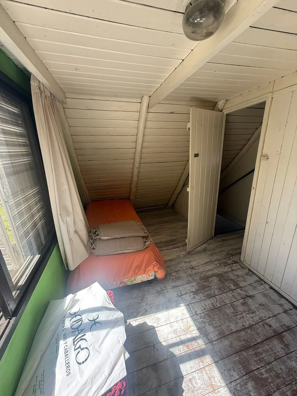 Primer dormitorio de planta alta, revestido en madera, con ventana amplia, cortinas y placard