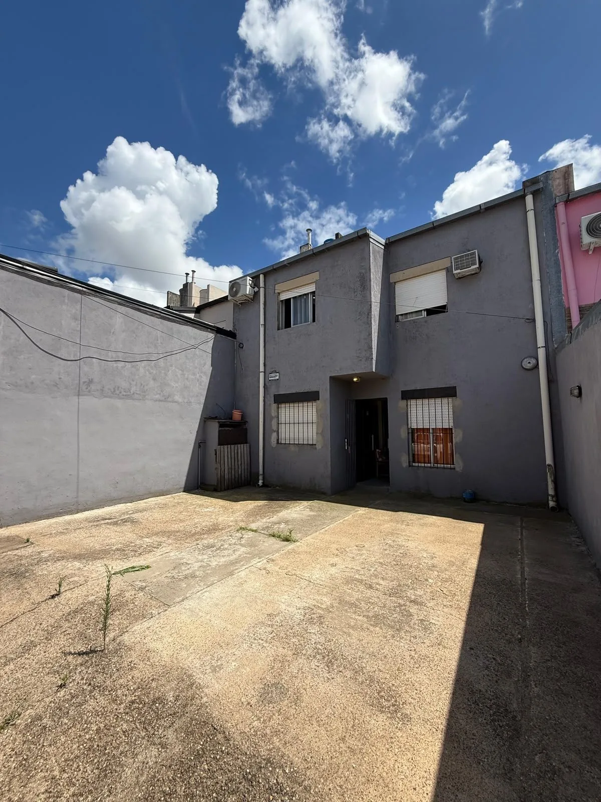 La casa desde la cochera: planta baja con rejas y planta alta con dos ventanas, una por dormitorio