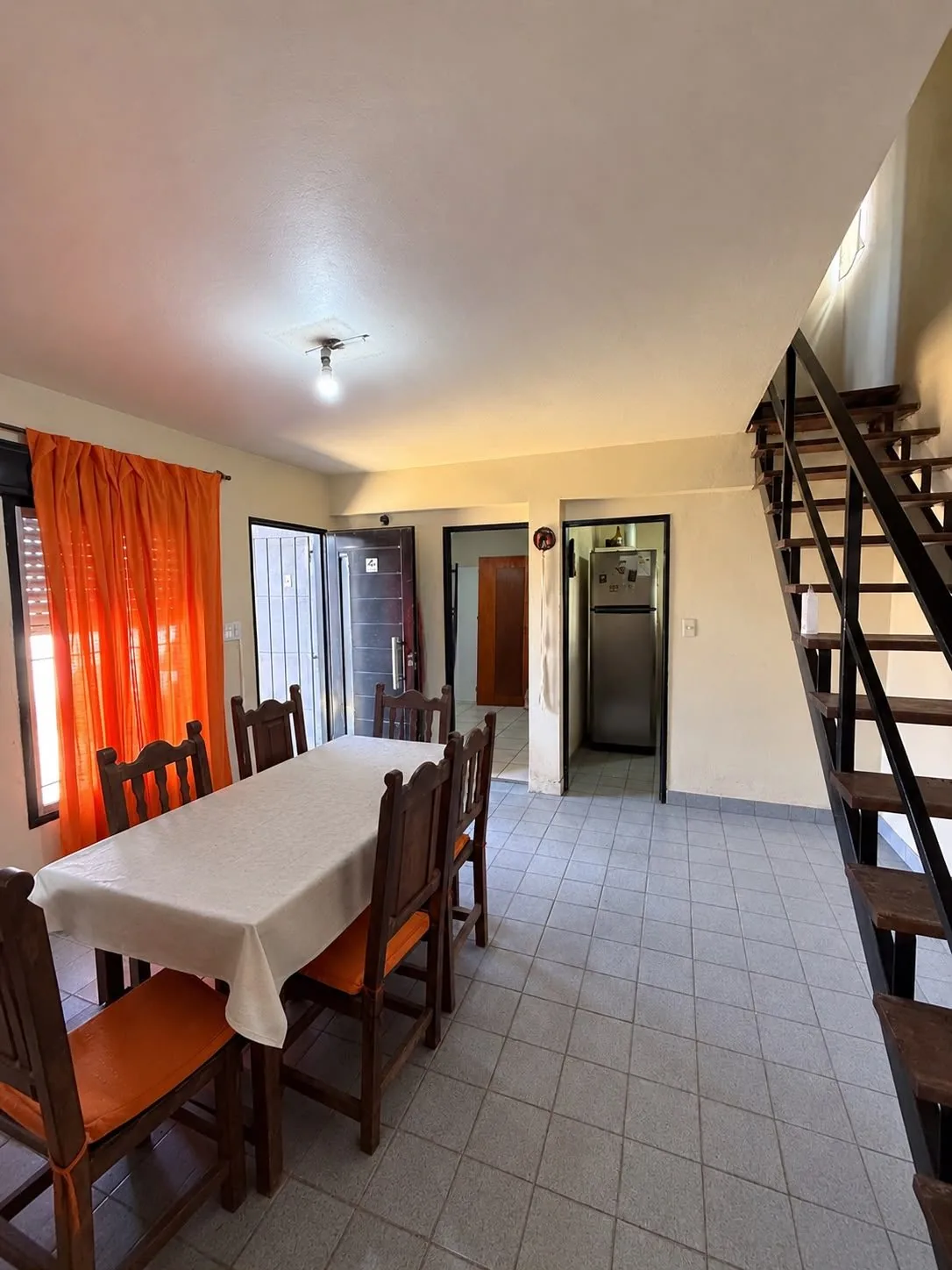 El living comedor, con la escalera de hierro y madera a la planta alta, la puerta de entrada y el paso a la cocina