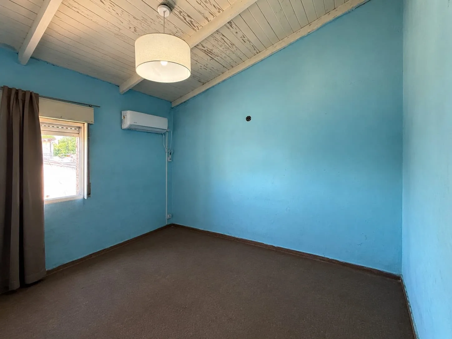 El segundo dormitorio, con techo de madera a la vista, aire acondicionado split y ventana con persiana