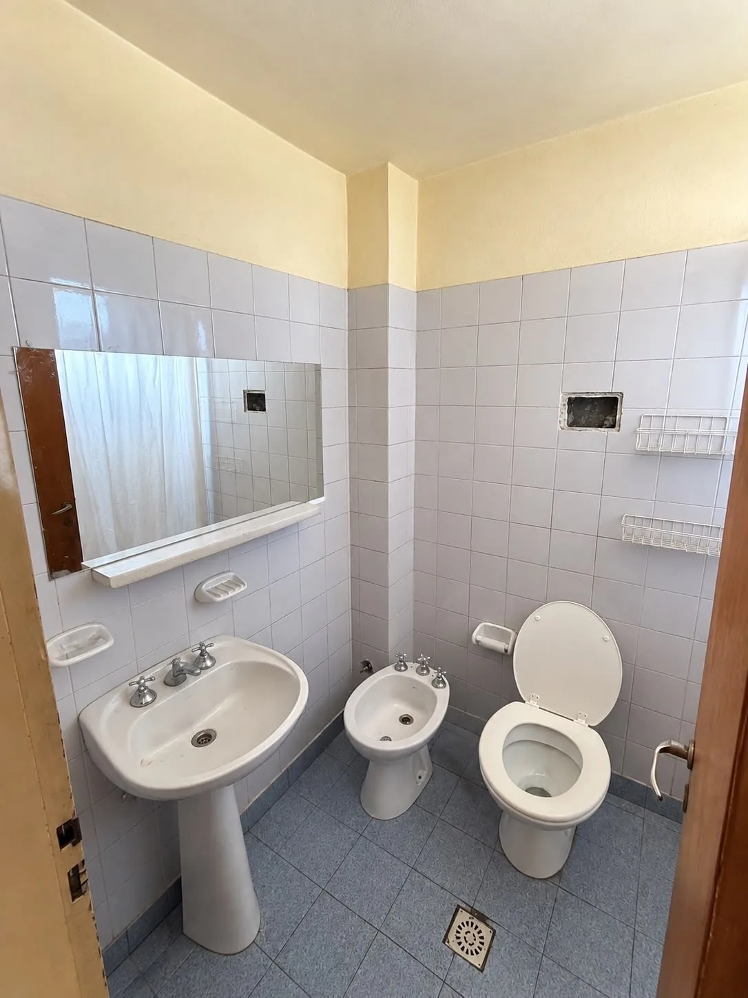 El baño, revestido en cerámica, con lavatorio de pie, inodoro, bidet y espejo
