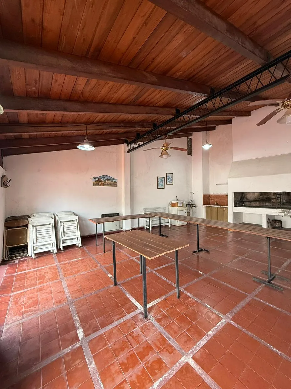 Otra vista del quincho, con techo de madera, mesas largas y sillas plegables