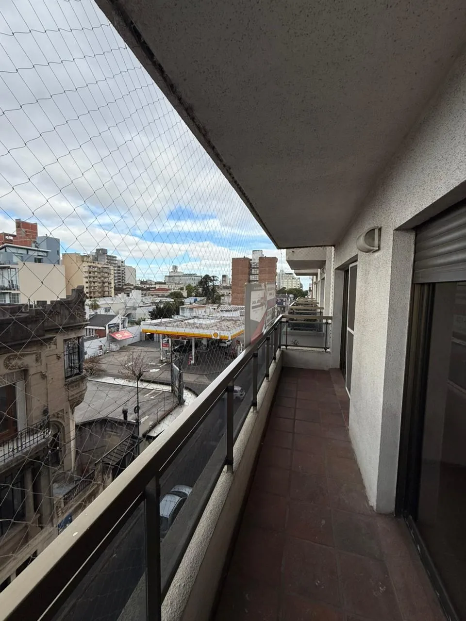 El balcón del frente, corrido, con baranda de vidrio, red de protección y piso cerámico