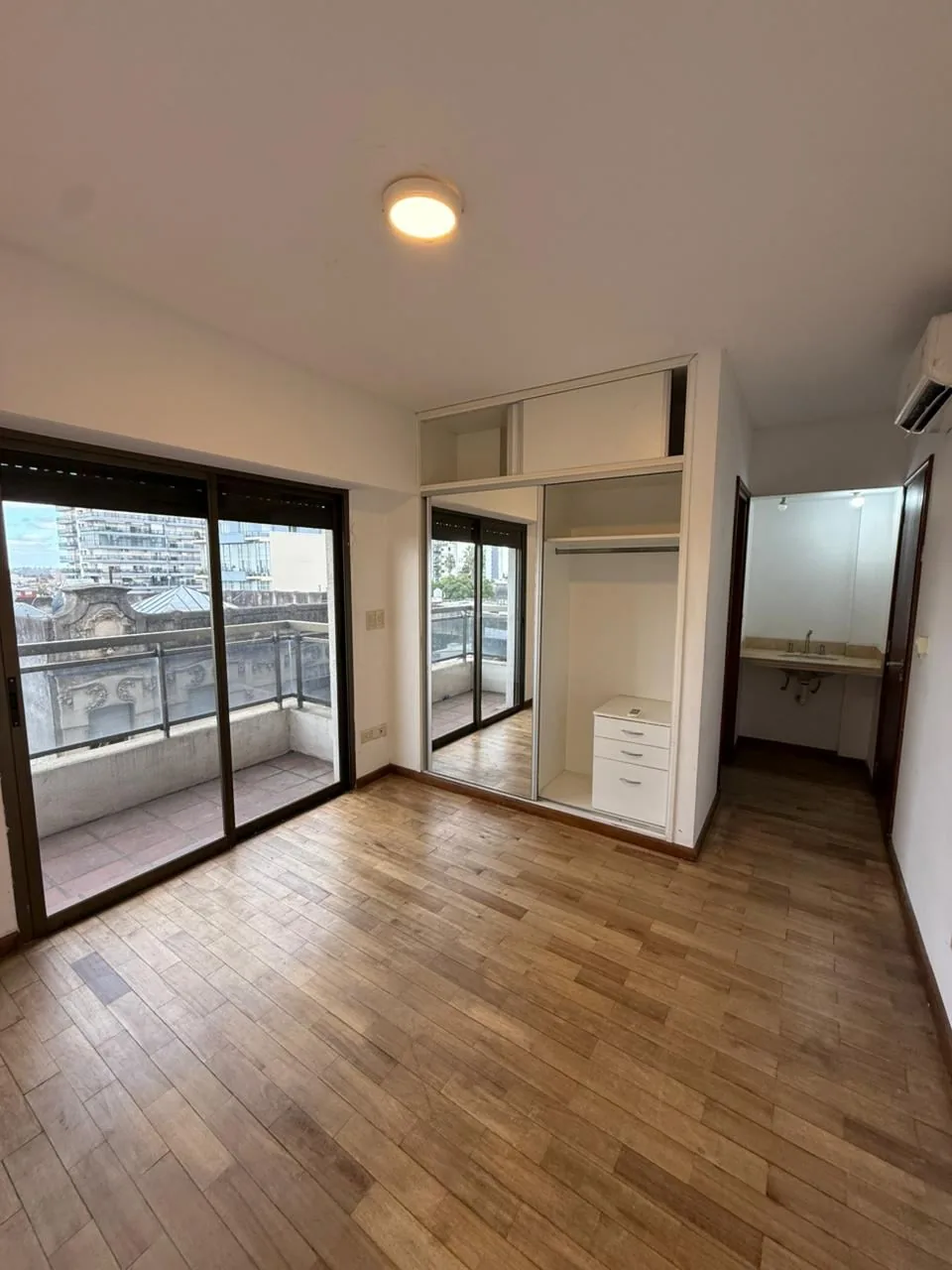 El dormitorio principal en suite: salida al segundo balcón, placard con puertas espejadas, aire acondicionado y el antebaño con lavatorio