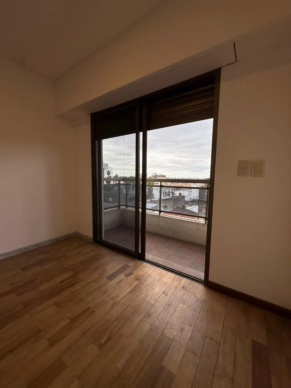 La puerta corrediza al balcón, con persiana eléctrica y piso de madera