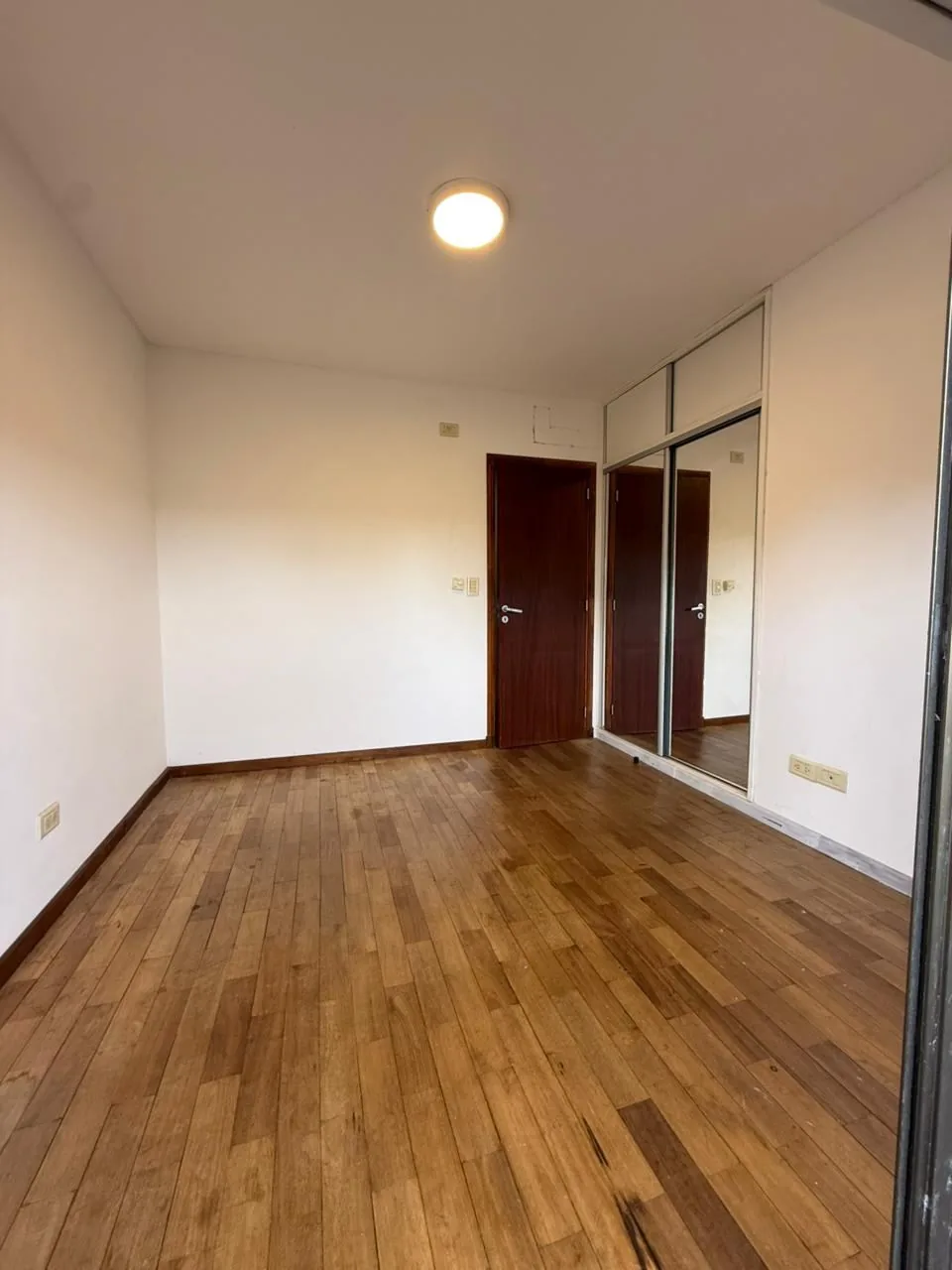 El tercer dormitorio hacia la puerta, con placard de puertas espejadas y piso de madera