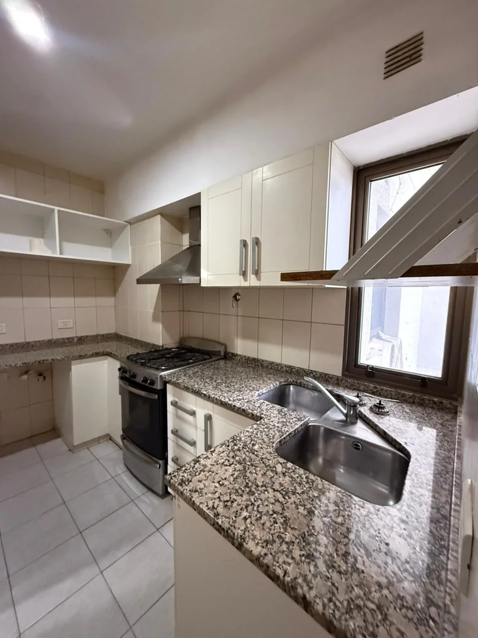 Cocina con mesada de granito en L, bacha doble de acero, campana y muebles altos y bajos