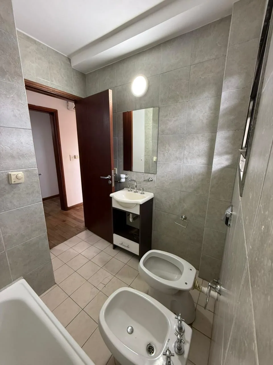 Baño completo con bañera, bidet y vanitory; en la pared, el termostato de la losa radiante individual