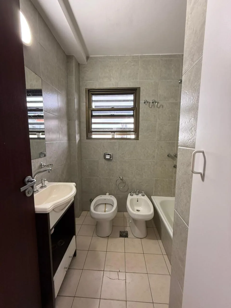 El mismo baño desde la puerta: inodoro, bidet, bañera y ventana con ventilación natural